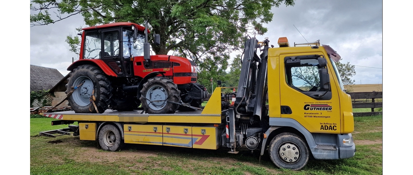 Tow truck, who lifts a large tractor from a rural area.