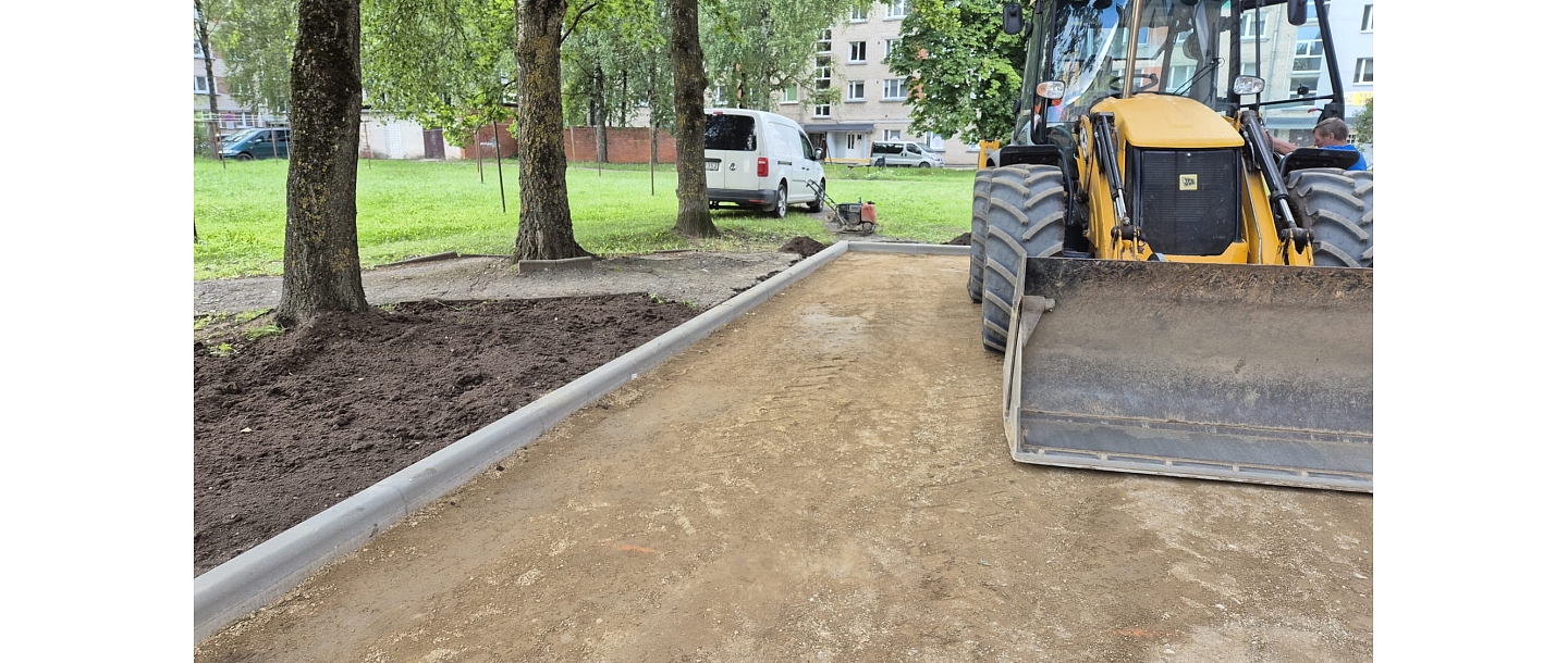 kskavators izlīdzina zemi ap jauniem ietves elementiem
